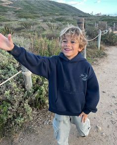 a young boy standing on a dirt road with his arms out in front of him