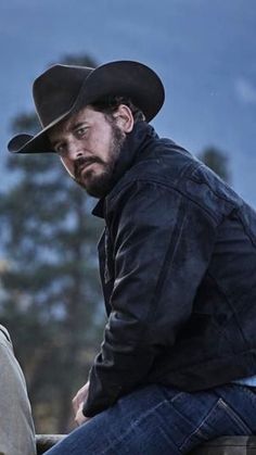 a man sitting on the back of a horse wearing a cowboy hat and looking off into the distance