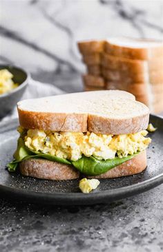 an egg and avocado sandwich is on a black plate next to some toasted bread