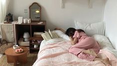 a woman laying in bed with her head on the pillow and reading a book next to an end table