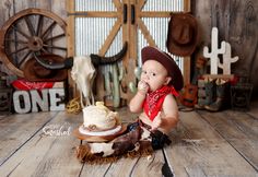 a baby sitting on the floor with a cake in front of him and wearing a cowboy hat