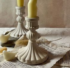 two white candles sitting on top of a table next to some papers and a bird