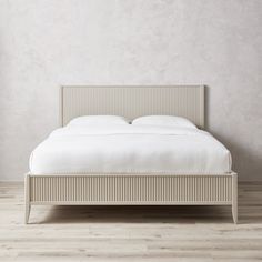 a bed with white sheets and pillows in a room that has wood flooring on it