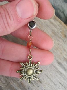 a person is holding a small sun charm in their left hand and wearing a ring with an orange bead on it