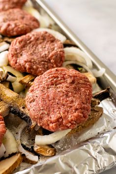 hamburger patties and onions on top of foil in a baking pan, ready to go into the oven