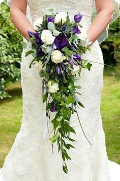 a woman in a wedding dress holding a bridal bouquet with purple and white flowers