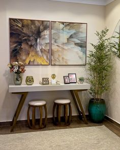 two paintings hang on the wall above a table with stools