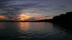 the sun is setting over the water and clouds are reflected in the water, with trees on either side