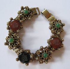 This is a wonderful vintage bracelet from the 1950's at my best estimate. This is a designer quality piece, but it is not marked or signed. Done in the style of Florenza, Art, and Goldette, this revival style bracelet features black and carnelian glass cabochons with Grecian gods or goddesses "carved" into the tops. These are probably molded glass intaglios. The black and carnelian stones are accented with green round ballotini, also glass. The bracelet is gold plated. The bracelet is 7 inches l Thomas Charley Jewelry, Luxury Intaglio Bracelets, Costume Jewelry Jubilee Bracelet, Vintage Round Bracelet With Jewels, Vintage Jeweled Bracelets For Collectible, Antique Jeweled Bracelet For Formal Occasions, Formal Metal Bracelet With Vintage Charm, Antique Metal Bracelet With Jewels, Formal Costume Jewelry Bracelet With Jewels