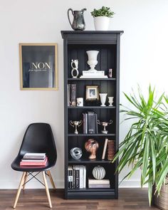 a black bookcase with books and plants on top