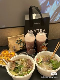 two bowls of soup with chopsticks next to a bag and some drinks on a table