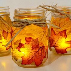 three mason jars filled with autumn leaves and twine tied to the lids, all lit up