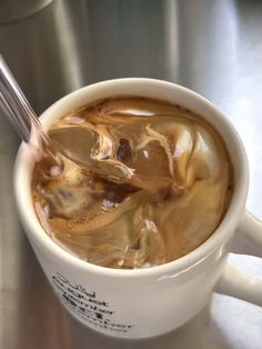 a cup filled with liquid and ice sitting on top of a metal counter next to a spoon