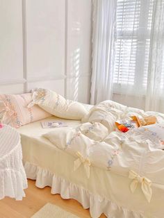 a bed with white ruffled bedspread and pillows on it in front of a window