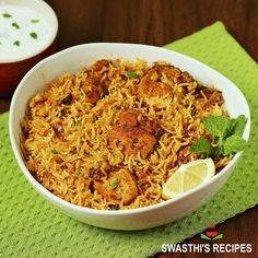 a white bowl filled with chicken biriyani next to a cup of yogurt