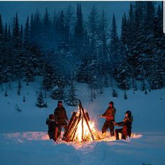 four people sitting around a campfire in the snow