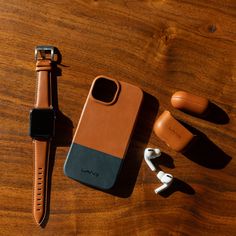 an iphone case, earbuds and headphones on a wooden table with a watch