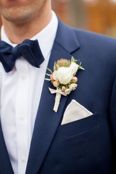 a man wearing a blue suit with a white rose boutonniere on his lapel