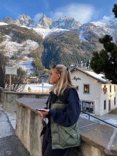 a woman is sitting on a wall looking at the snow covered mountains in the background