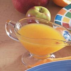 an orange juice in a pitcher next to apples and other fruit on a wooden table