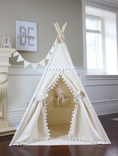 a teepee with white pom poms on it and a baby's room in the background