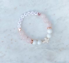 This beautiful personalized beaded bracelet is made with Rose Quartz ( Pink), Aquamarine (Blue) or Alabaster (White),  Howlite Cross and copper beads.   These bracelets are the perfect addition for your special occasion as a favour for a baptism, christening, communion, wedding shower, confirmation or any special or religious occasion.   DETAILS: ♡ Each bracelet comes with letter beads, 10 to 12 - 10MM beads and a Howlite Cross.  ♡ Select bracelet size in drop down.  Custom sizes available, specify in personalization section.  Select size or measure your wrist and add between 1/4 to 1/2 inch depending on your preference. ♡ Made with White Alabaster and Aquamarine or Rose Quartz beads and copper details. ♡ Each bracelet comes packaged beautifully with a jewellery bag. Great as a favour or a Mother's Day Pink Name Bracelet, Customized Pink Beaded Bracelets For Birthday Gift, Personalized Pink Spiritual Bracelets, Customized Pink Beaded Bracelets For Birthday, Personalized Name Bracelet In Pink, Customized White Jewelry For Birthday, Personalized Pink Spiritual Bracelet, Pink Beaded Bracelet With Name, Spiritual Personalized Pink Bracelets