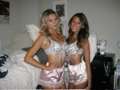 two beautiful young women standing next to each other in front of a bed with white sheets