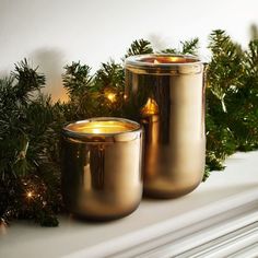 two gold candles sitting on top of a mantle next to evergreen branches and christmas lights