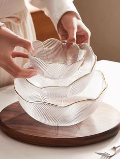 a person is placing something in a glass bowl on a wooden platter with utensils