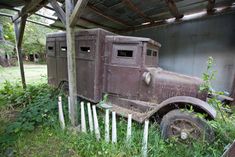 an old truck sitting in the grass under a wooden structure with vines growing out of it