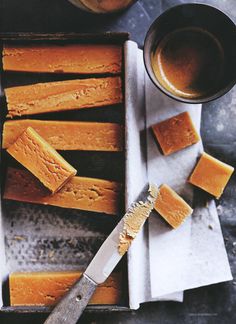 several pieces of cake sitting on top of a pan next to two cups and a knife