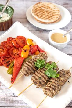 grilled meat and vegetable skewers on a white plate with pita bread