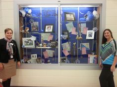 two women standing in front of a display case with pictures and other items on it