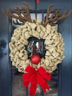 a christmas wreath with reindeer antlers and a red ball hanging from the front door