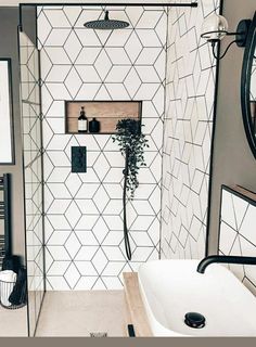 a white and black tiled bathroom with a sink, shower head, mirror and towel rack