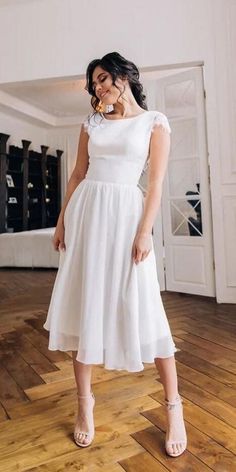 a woman standing on top of a wooden floor wearing a white dress and sandals with her hand in her mouth