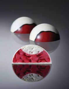 two red and white desserts sitting on top of a reflective surface, with one being sliced in half