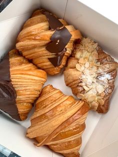 four pastries in a box with chocolate and almonds on the top one has a bite taken out of it