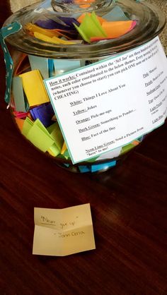 a jar filled with colorful origami pieces next to a piece of paper on top of a wooden table