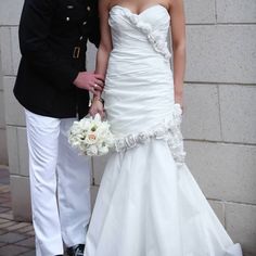 a bride and groom standing next to each other in front of a brick wall holding hands