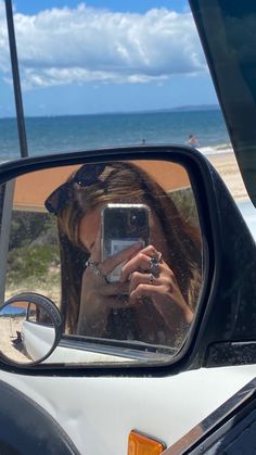 a woman taking a selfie in the side view mirror of a car near the beach