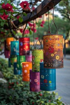 colorful tin can lights hanging from a wooden beam in front of some bushes and flowers