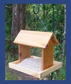 a bird feeder hanging from the side of a tree in front of some trees and grass