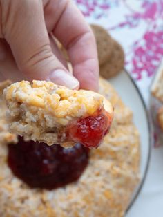 a hand holding a piece of food over a cracker with jelly on it and oatmeal in the background