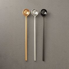 three spoons are lined up next to each other on a gray surface with silver and gold accents