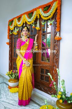 a woman in a yellow and pink sari standing next to a doorway with flowers