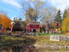 people are walking around in front of a red house and water pond with fall foliage