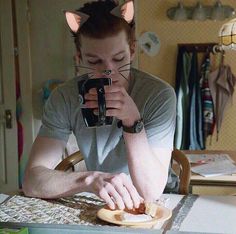 a man sitting at a table with a sandwich in front of him while holding a camera