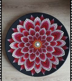 a red and white flower painted on a black plate with polka dot border around it