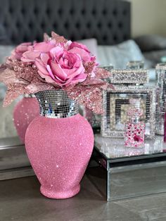 a pink vase sitting on top of a table next to a mirror box and flowers